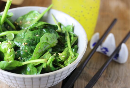 Japanese spinach and sesame salad on a wooden table with chop sticks and a drink